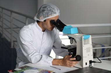 Young man in lab coat examines something under a microscope