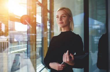 Young woman looks out a window while holding laptop