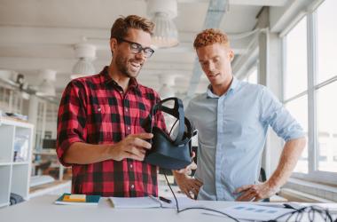 Two young men chat while holding a virtual reality headset