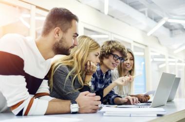 Young employees gather together to look at a laptop screen